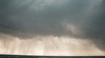 A dramatic sky with dark clouds and heavy rain over the sea, indicating stormy weather conditions