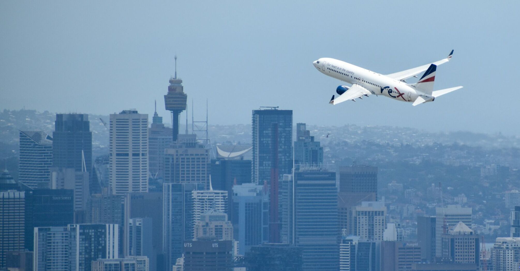 Rex Airlines aircraft taking off with city skyline in the background