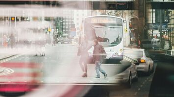 View of a busy city street with a bus and pedestrians through a window with reflections