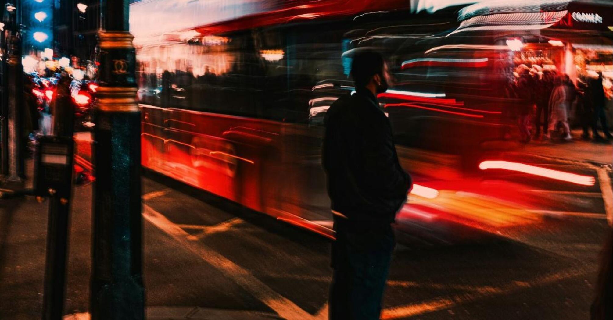 Blurred image of a red double-decker bus at night in a busy city street
