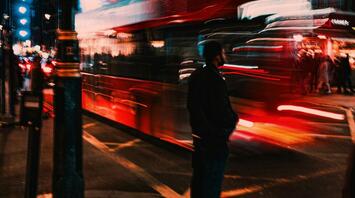 Blurred image of a red double-decker bus at night in a busy city street