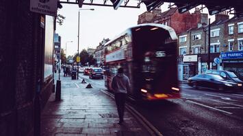Blurred image of a red double-decker bus moving along a street with a pedestrian walking on the sidewalk