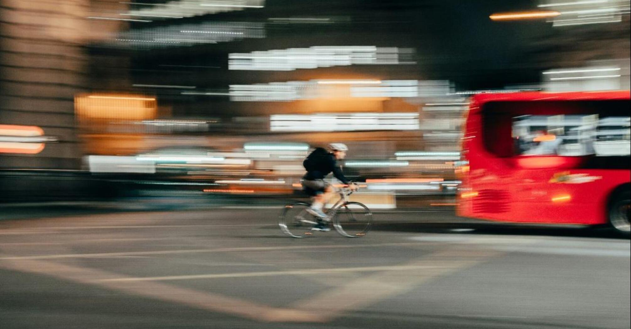A cyclist riding past a red bus at night in a city with blurred lights