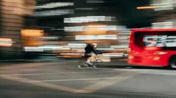 A cyclist riding past a red bus at night in a city with blurred lights