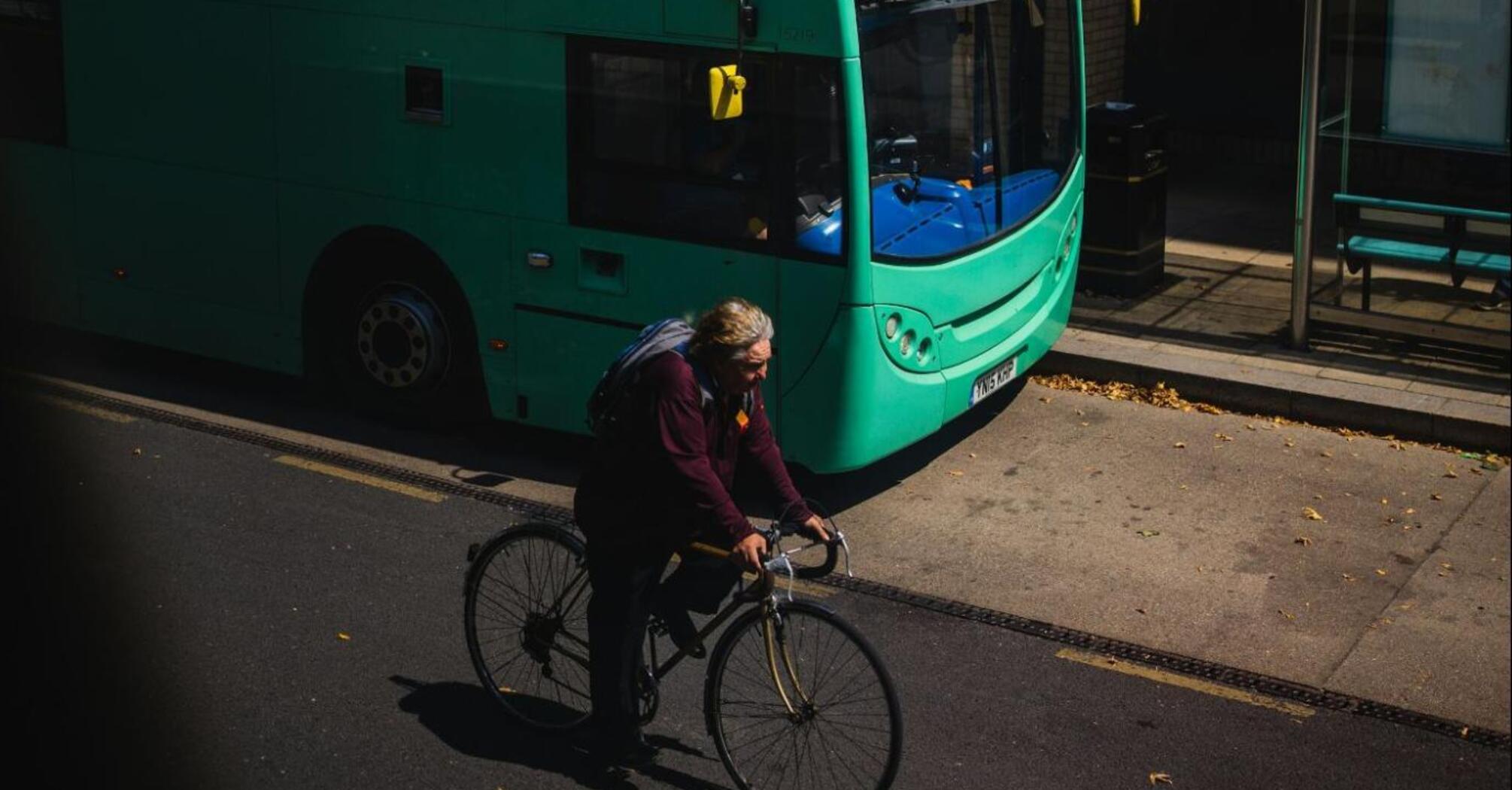 Cyclist riding past a green double-decker bus at a bus stop