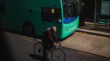 Cyclist riding past a green double-decker bus at a bus stop