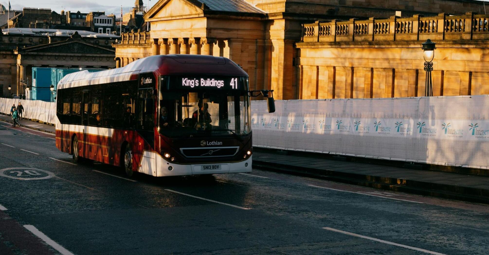A Lothian bus driving through Edinburgh, with historical architecture in the background