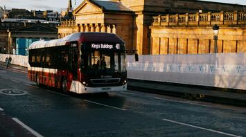A Lothian bus driving through Edinburgh, with historical architecture in the background