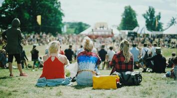Three people at a festival sitting with their backs to the stage
