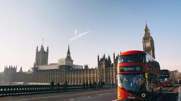 Red double decker bus passing the bridge in front of Palace of Westminster in London