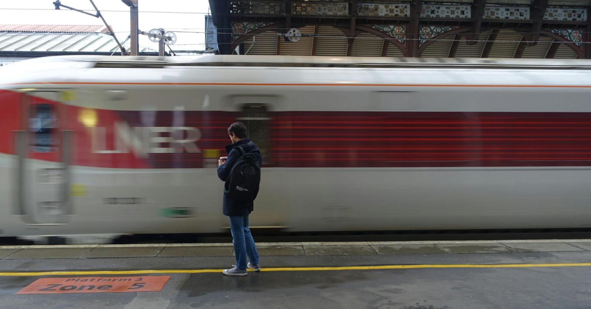 A person stands on a train platform as an LNER train passes by at high speed