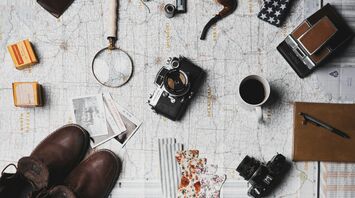 Travel essentials laid out on a map, including a camera, magnifying glass, boots, and a coffee cup