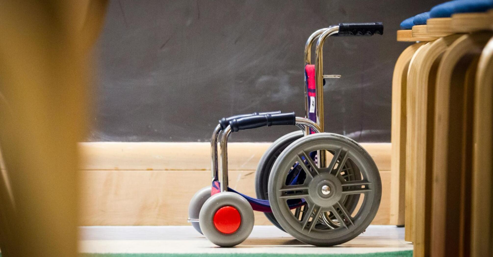 Small wheelchair next to wooden chairs in classroom