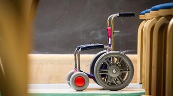 Small wheelchair next to wooden chairs in classroom