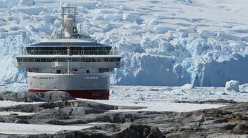 A cruise ship in front of a glacier with a penguin in the foreground