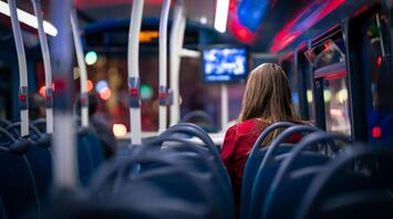A woman sits alone on a nearly empty bus at night, with city lights visible through the windows