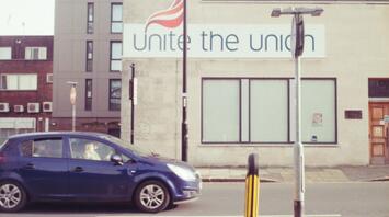 A blue car passing by a building with a large 'Unite the Union' sign