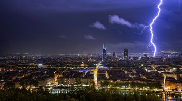 A dramatic lightning strike illuminates the night sky over Lyon, highlighting the skyline and buildings below