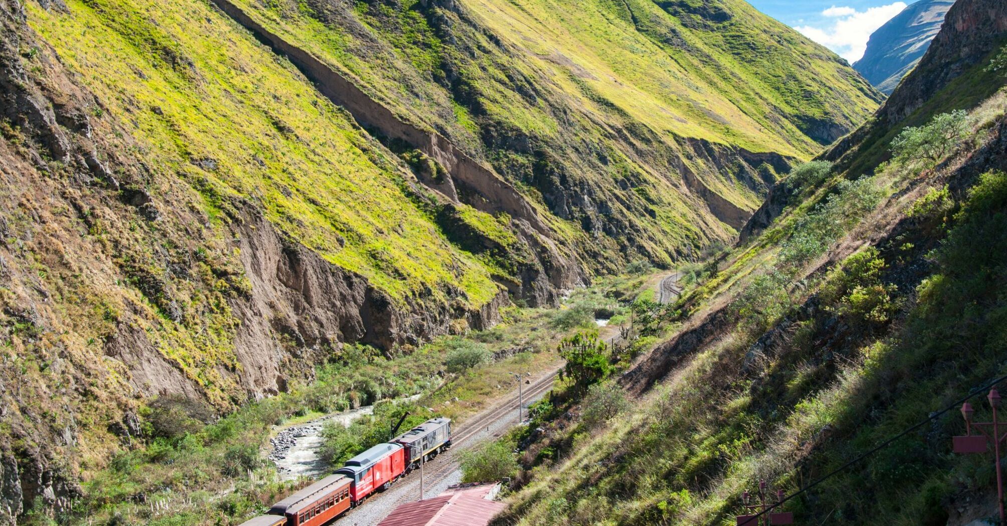 train on railway between green mountains during daytime