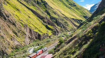 train on railway between green mountains during daytime