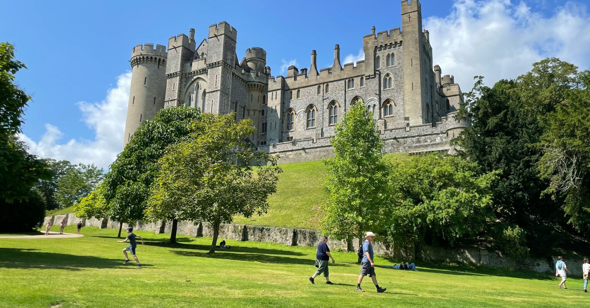 A view of Arundel Castle with people walking on the grass in front of it on a sunny day