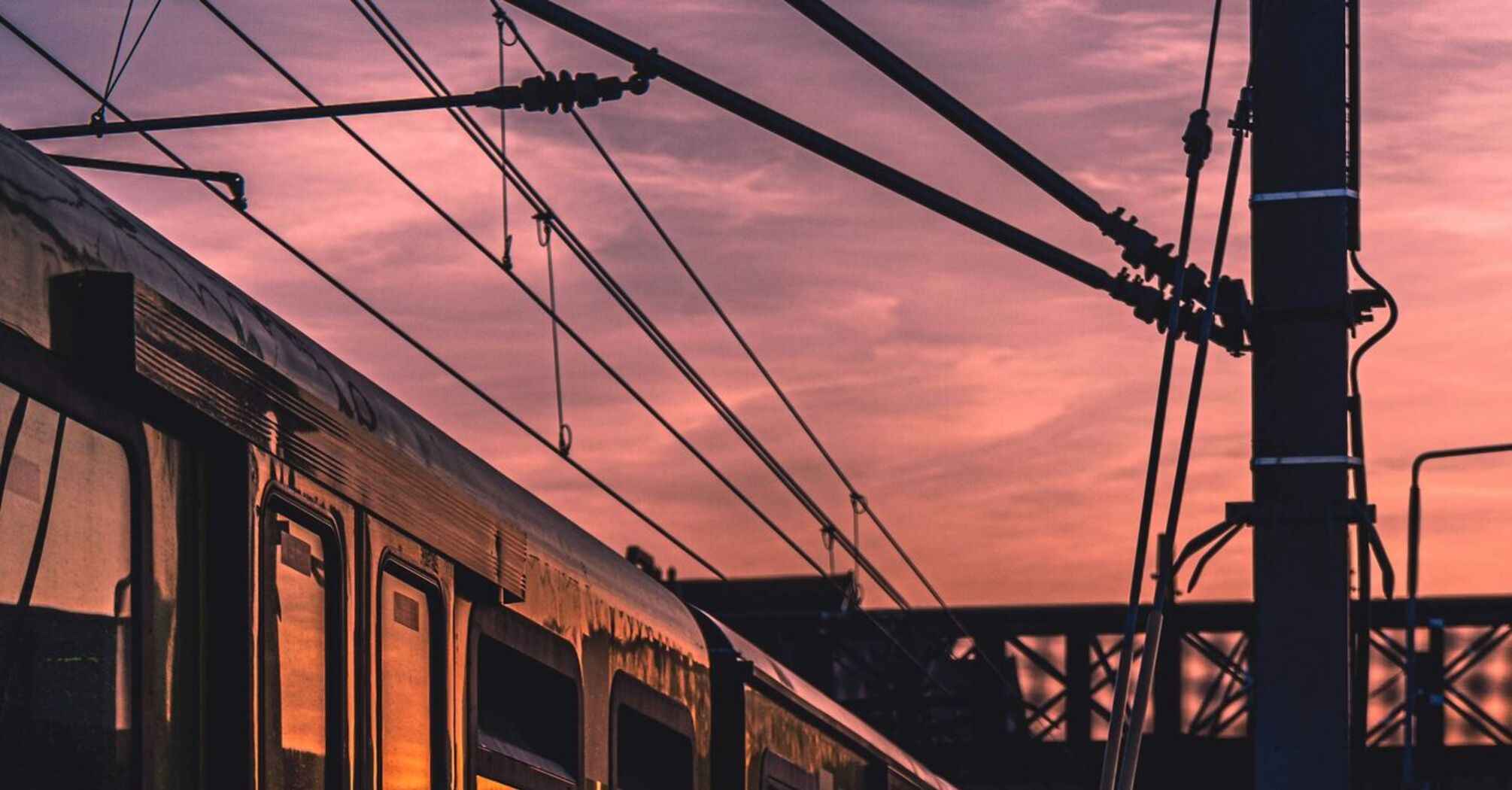 A train at a station during sunset with overhead cables visible