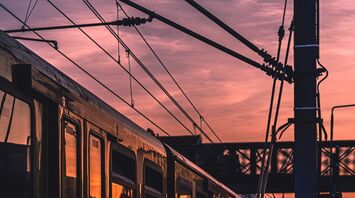 A train at a station during sunset with overhead cables visible