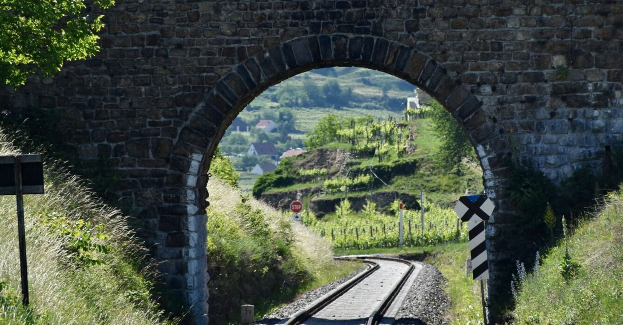 Stone bridge over railway tracks in a lush green valley with distant hills