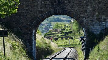 Stone bridge over railway tracks in a lush green valley with distant hills