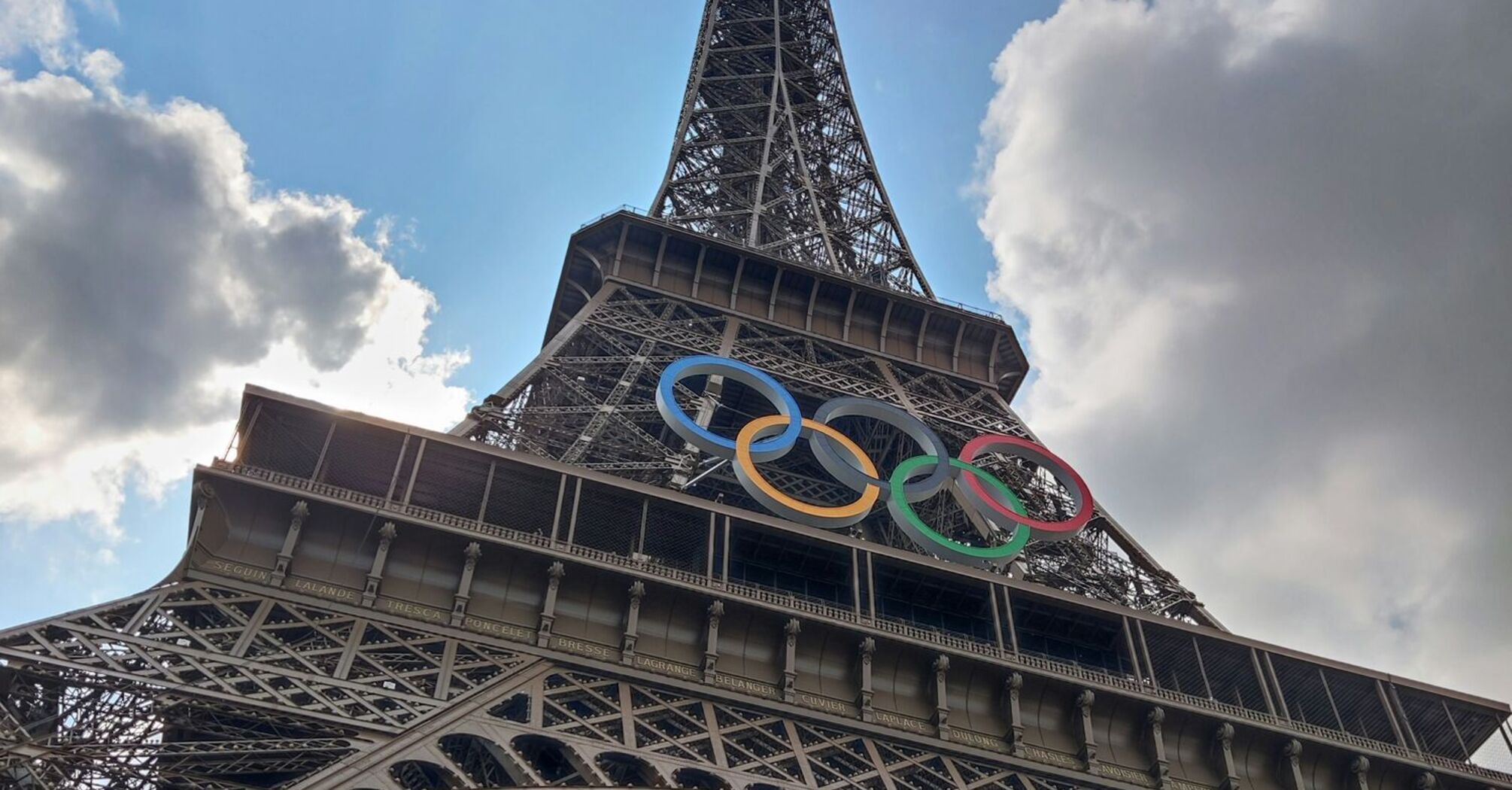 The Eiffel Tower with Olympic rings under a partly cloudy sky in Paris