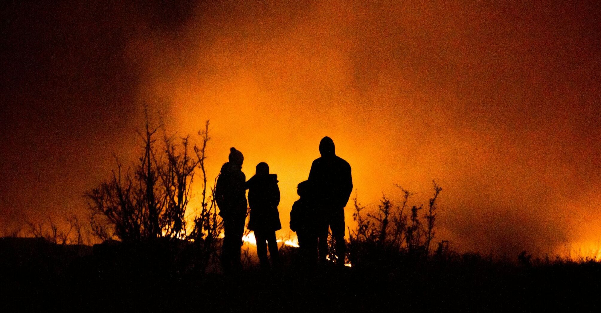 Silhouetted figures standing near intense wildfire at night