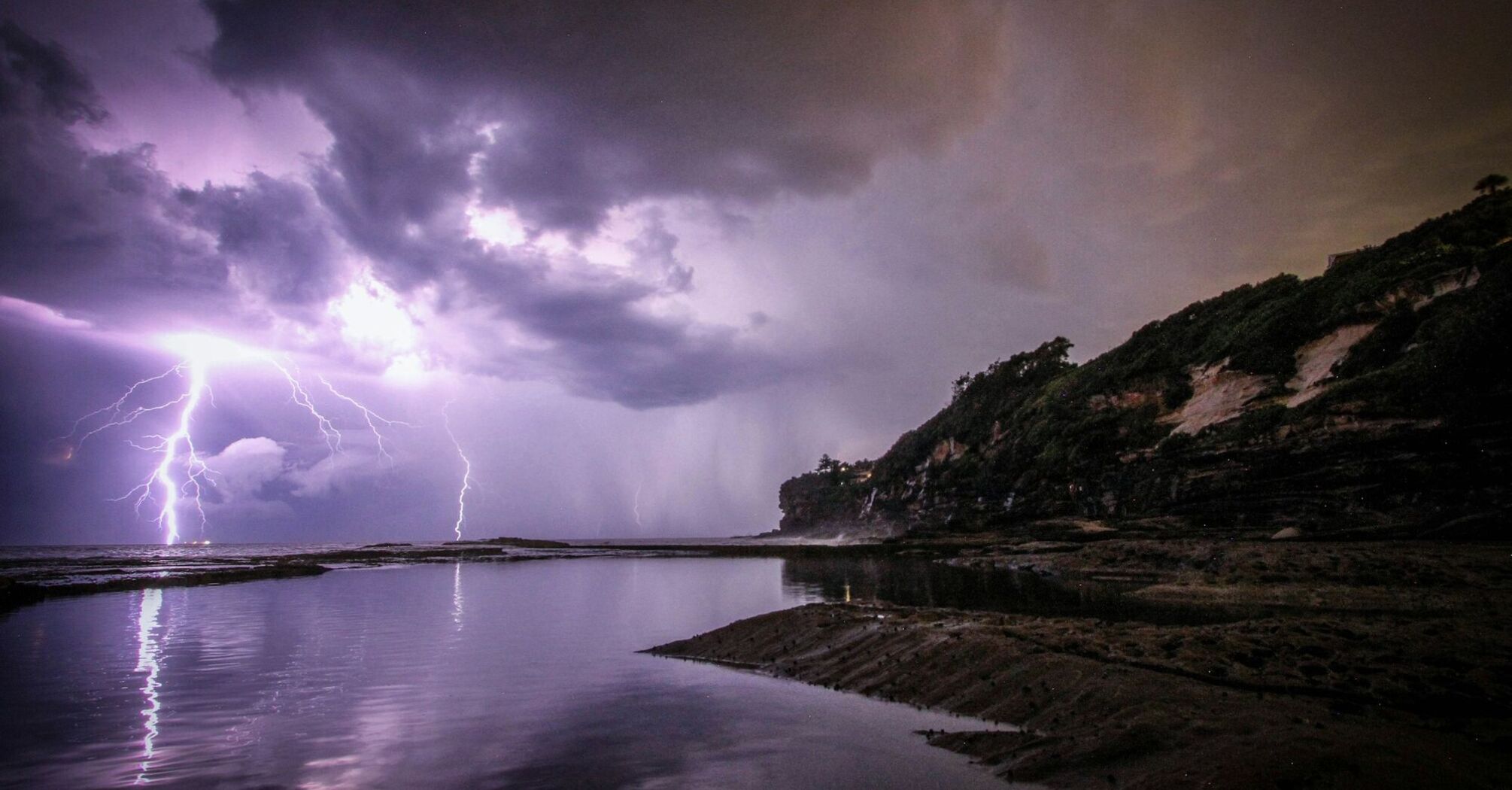 A dramatic coastal scene with lightning striking over the ocean, illuminating the night sky with intense, stormy clouds