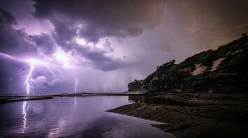 A dramatic coastal scene with lightning striking over the ocean, illuminating the night sky with intense, stormy clouds