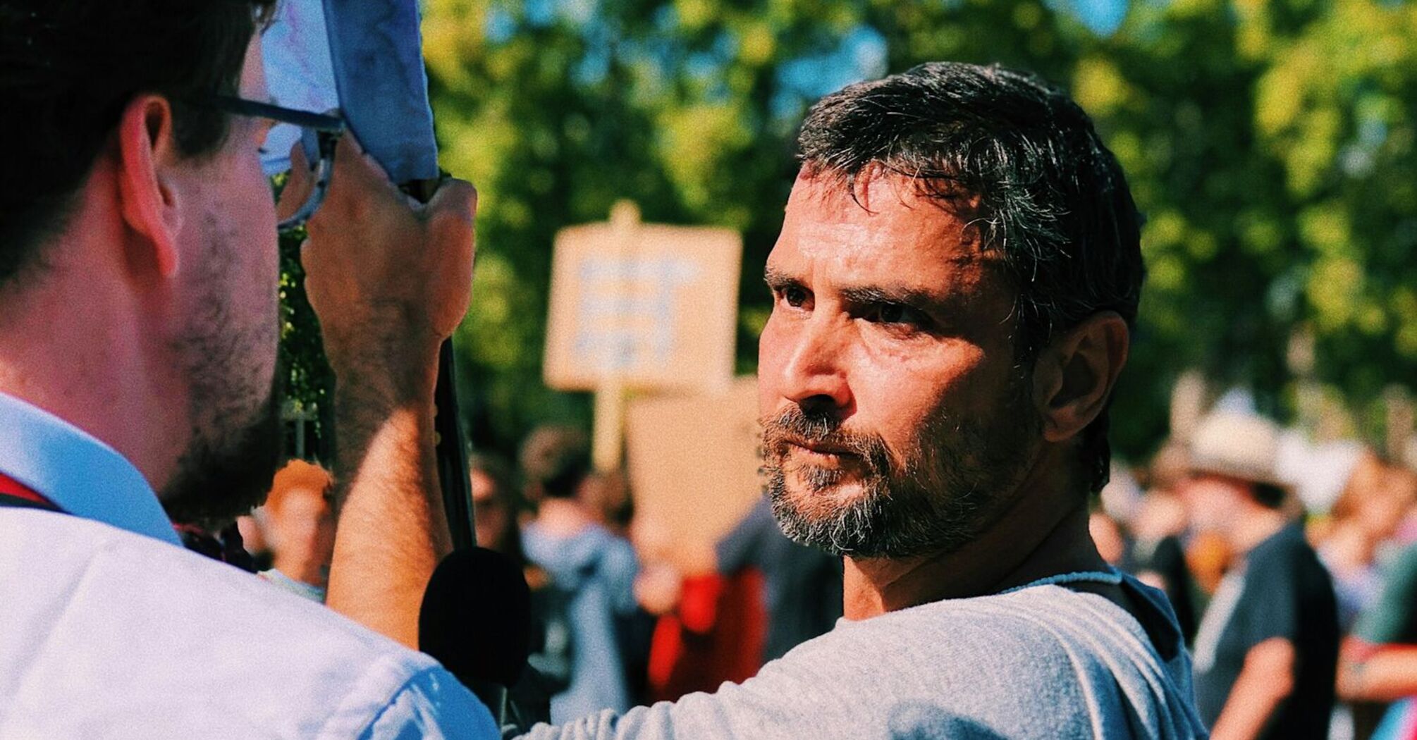 A man holding a sign during a protest, engaging in conversation with another person