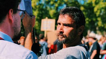 A man holding a sign during a protest, engaging in conversation with another person