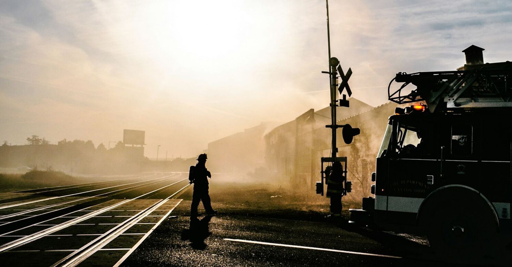 Firetruck and firefighter near a railway crossing in a smoky environment during sunrise