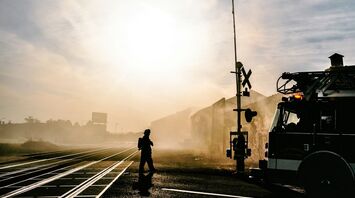 Firetruck and firefighter near a railway crossing in a smoky environment during sunrise