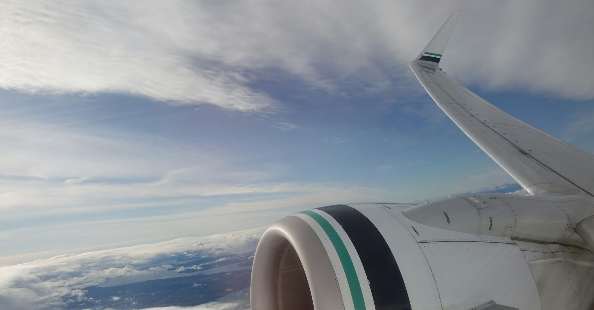 View of an Alaska Airlines plane wing and engine during flight with clouds and sky in the background