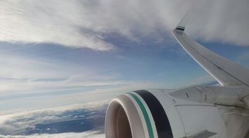 View of an Alaska Airlines plane wing and engine during flight with clouds and sky in the background