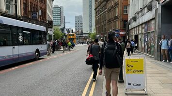 A busy street in Manchester with pedestrians walking alongside buildings and buses driving on the road