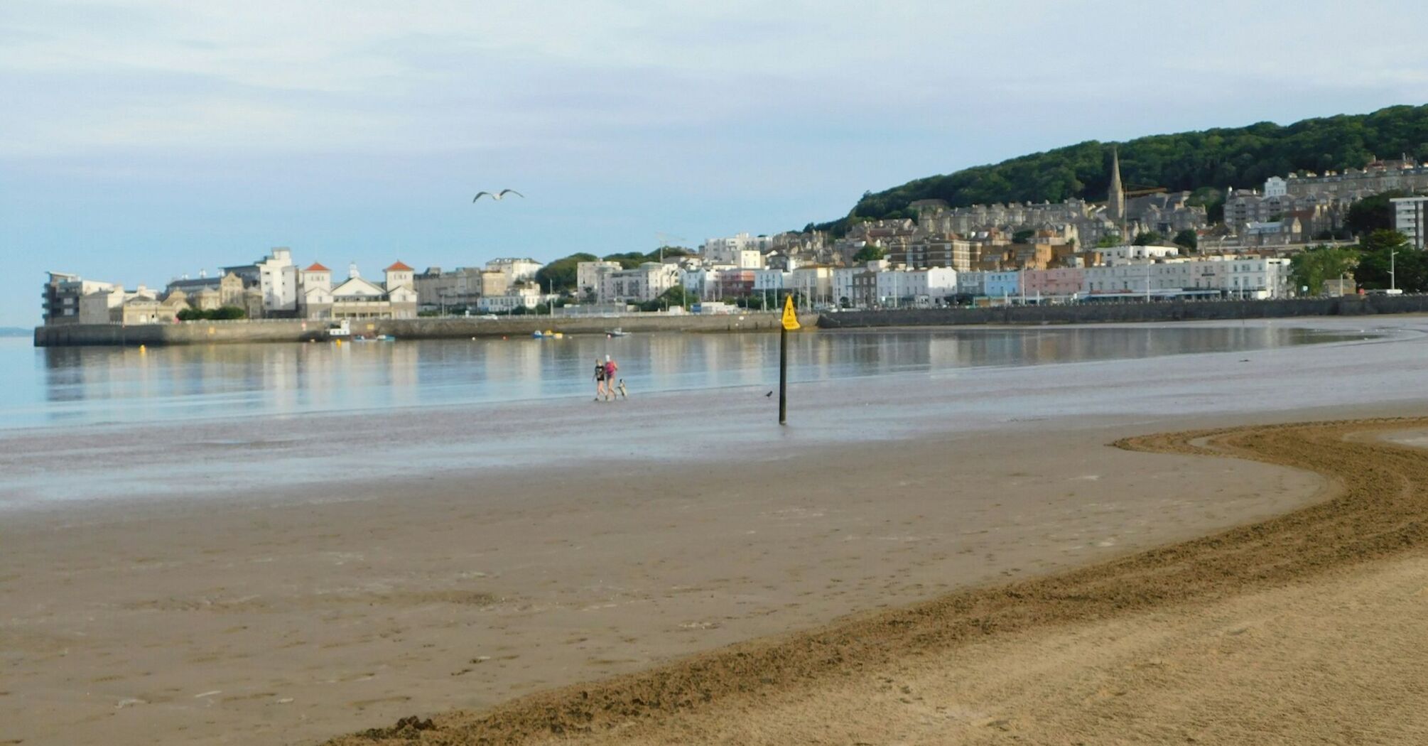 A empty beach with a town in the background and a few people walking along the shoreline