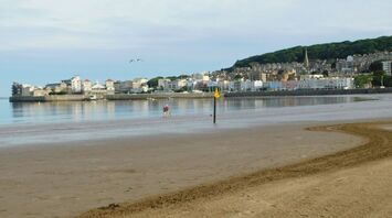 A empty beach with a town in the background and a few people walking along the shoreline