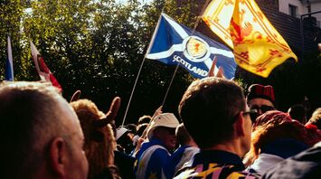 A crowd of football fans in Scotland, waving Scottish flags in a festive atmosphere