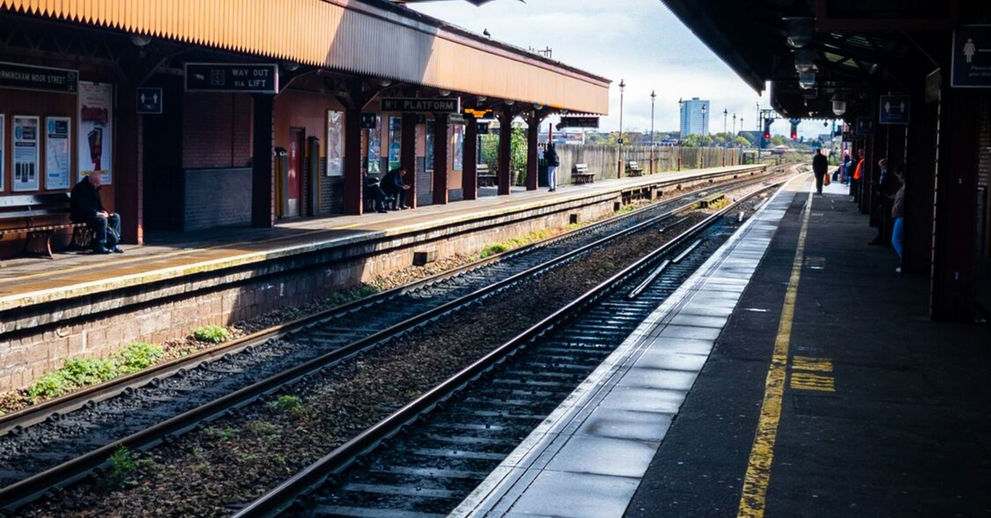 A nearly empty railway station platform in Birmingham with tracks and an overpass bridge in view