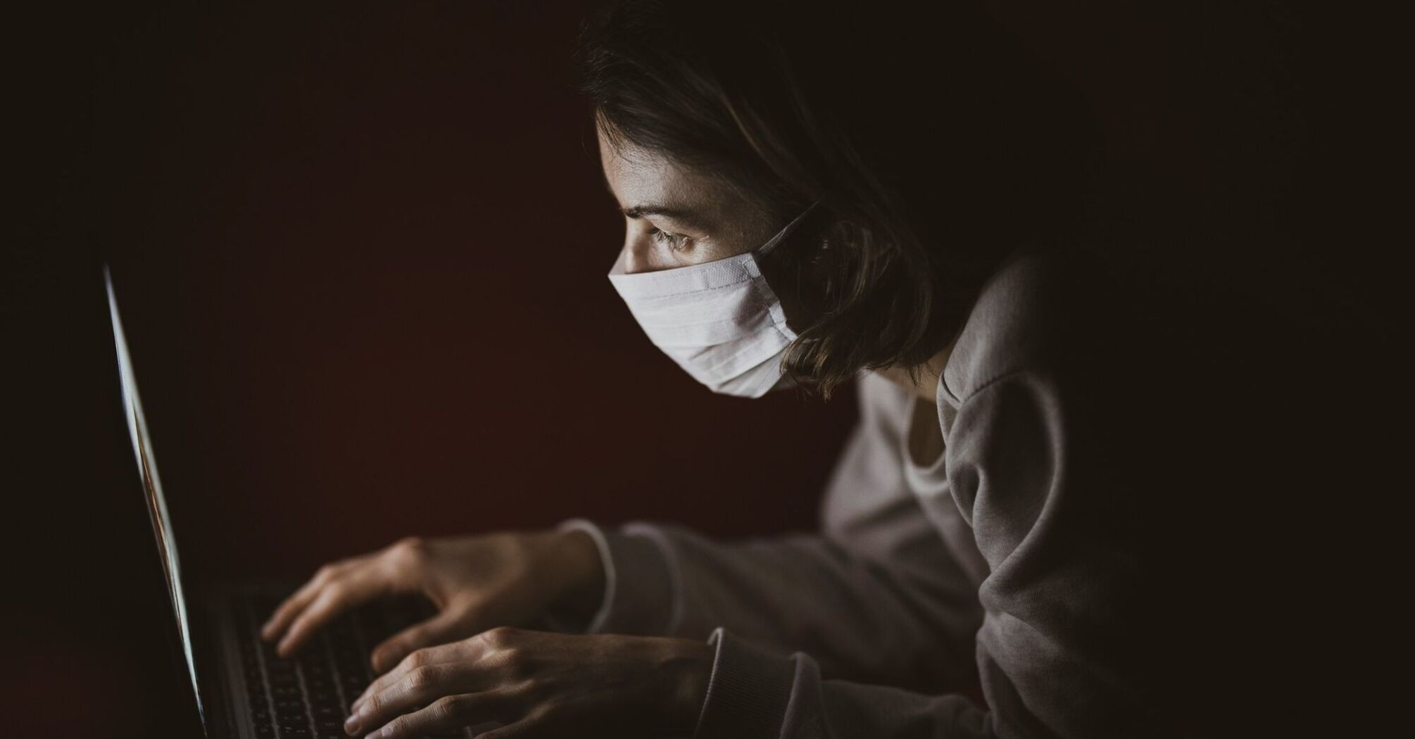 Person wearing a mask while using a laptop in a dimly lit environment