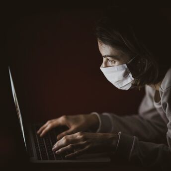 Person wearing a mask while using a laptop in a dimly lit environment
