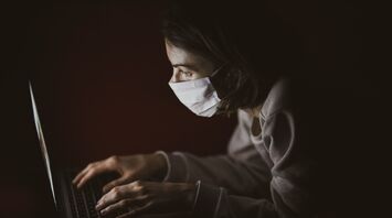 Person wearing a mask while using a laptop in a dimly lit environment