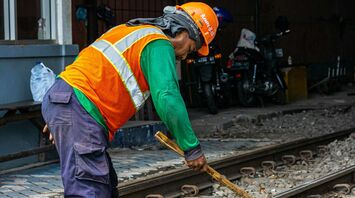 A railway worker in a high-visibility vest and helmet uses a hammer to work on railway tracks during maintenance