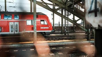 A red regional train stands idle on the tracks under a steel railway bridge, highlighting the temporary disruptions on the Berlin-Hamburg route