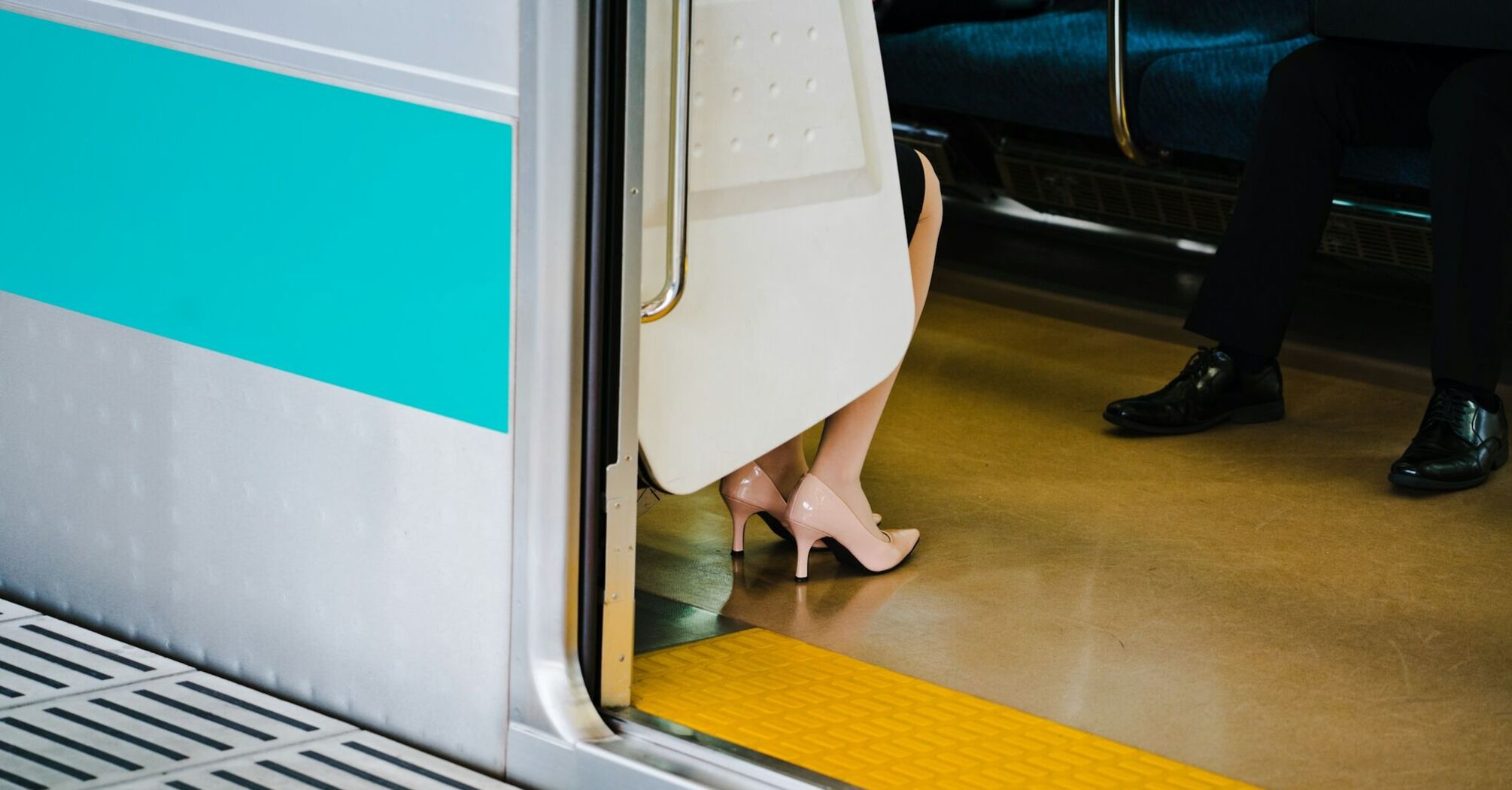 A woman’s legs in heels visible while seated inside a train, with the train door open